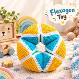 May include: A crocheted flexagon toy featuring a geometric ring shape with alternating yellow and turquoise triangular segments separated by white borders. The toy has a textured yarn surface and is displayed in a bright, indoor setting.