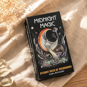 May include: A rectangular black tarot deck box titled Midnight Magic with a crescent moon shaped mushroom illustration, smaller mushrooms, and the text Atarot Deck of Mushrooms by Sara Richard printed in white and yellow on the front cover.