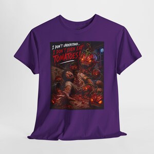 May include: A purple short-sleeve t-shirt featuring a graphic print of a person being attacked by glowing, sharp-toothed tomatoes in a kitchen. The text above the scene reads, I DON'T UNDERSTAND... I DON'T EVEN EAT TOMATOES! in white and red.
