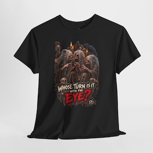 May include: A black t-shirt featuring a graphic illustration of three elderly figures with long grey hair, holding a single eyeball. The text reads, WHOSE TURN IS IT WITH THE EYE? The design includes candles, skulls, and a raven in a dark, moody style.
