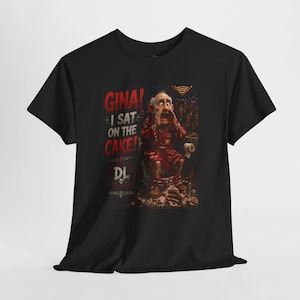 May include: A black short-sleeved t-shirt featuring a graphic print of an elderly person in a red robe sitting on a cake. The text reads GINA! I SAT ON THE CAKE! with a DL logo and skull icon. The design includes a dark background and red lettering.