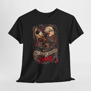 May include: A black short-sleeved t-shirt featuring a graphic print of a small figure with large eyes riding a moth. The design includes a full moon, dark forest elements, and a banner with the text "NOT ALL WHO WANDER ARE SANE" in red and black.