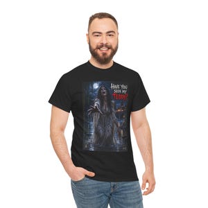 May include: A black short-sleeve t-shirt featuring a graphic print of a ghostly figure emerging from dark water at night. The figure has long dark hair and wears a tattered white gown. The text "HAVE YOU SEEN MY TEDDY?" is printed in white and red.