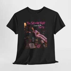 May include: A black short-sleeved t-shirt featuring a graphic print of a doll in pink pajamas lounging with various bottles and glasses. The text reads: The Saturday Night I have no life Party. Pajamas & low standards. Things I'm my tomorrow's problem.