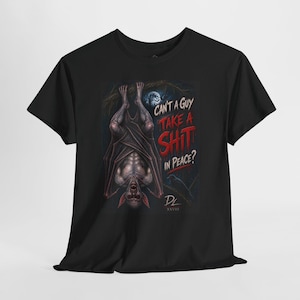 May include: A black short-sleeve t-shirt featuring a graphic of a bat hanging upside down from a branch. The text reads, "CAN'T A GUY TAKE A SHIT IN PEACE?" in red and white lettering. A full moon and dark forest background are visible behind the bat.