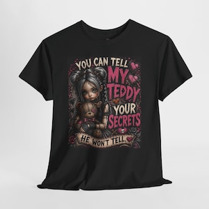 May include: A black short-sleeve t-shirt featuring a graphic of a girl with pigtails holding a stitched teddy bear. The text reads: YOU CAN TELL MY TEDDY YOUR SECRETS HE WON'T TELL. The design includes pink hearts, roses, and skull accents.
