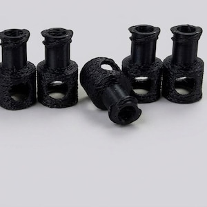 May include: A set of five black plastic cord locks, each featuring a cylindrical base with a textured surface and a central hole, topped with a smaller neck section. These functional fasteners are designed to secure drawstrings on clothing or bags.