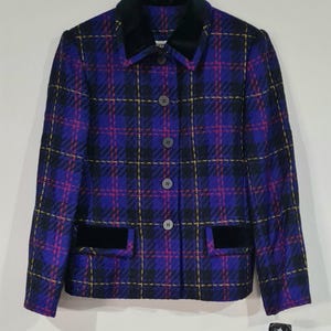 May include: A long-sleeve jacket featuring a vibrant purple, black, and magenta plaid pattern. The garment includes a solid black velvet collar, matching black velvet pocket flaps, and a front button closure with four dark circular buttons.