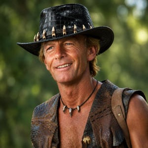 Può includere: Un cappello in pelle nera con texture a coccodrillo caratterizzato da una fascia decorata con una serie di ornamenti bianchi a forma di dente. Una collana di corda scura con tre ciondoli a forma di dente poggia sul petto, abbinata a un gilet in pelle marrone.