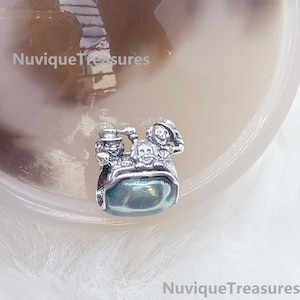 Könnte beinhalten: Ein silberfarbener Charm-Anhänger mit drei skulptierten Figuren, die Hüte tragen, über einem glatten, durchscheinenden, blaugrünen ovalen Stein. Der Text NuviqueTreasures ist in der oberen linken und unteren rechten Ecke des Bildes zu sehen.