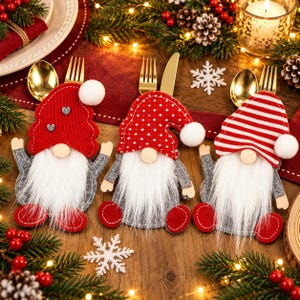 May include: Three gnome-shaped felt cutlery holders with white faux fur beards and wooden noses. Each features a unique hat: one solid red with two small hearts, one red with white dots, and one red and white striped. Each hat has a white pom-pom.