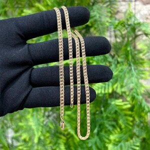 May include: A gold-toned chain necklace featuring a woven, mesh-like link design. The chain is composed of multiple interconnected metal loops that create a flexible, tubular structure with a polished finish and a secure clasp at the end.