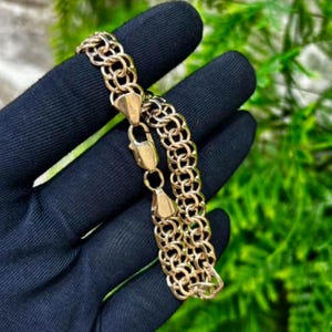 Può includere: Un bracciale a catena color oro caratterizzato da un complesso design a maglie circolari intrecciate. Il bracciale è costruito con una serie di anelli metallici intrecciati ripetuti e include una chiusura a moschettone sicura.