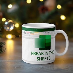 Może przedstawiać: Biały ceramiczny kubek z nadrukiem interfejsu arkusza kalkulacyjnego, zieloną kwadratową ikoną oraz napisem "FREAK IN THE SHEETS" pogrubionymi zielonymi wielkimi literami. Kubek posiada standardowe ucho i ma cylindryczny kształt.