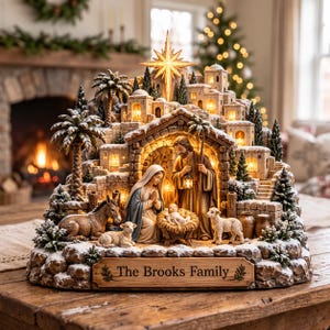 May include: A detailed nativity scene figurine featuring a central stable with a family, a donkey, and sheep. The structure includes illuminated stone buildings, palm trees, and a glowing star on top. A wooden plaque at the base reads The Brooks Family.