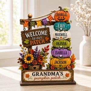 Könnte beinhalten: Ein dekoratives Tischschild mit einem Stapel aus sechs bunten Kürbissen mit Namen, einem Holzschild mit der Aufschrift WELCOME to our PATCH, einer Wimpelkette und einem Sockel mit der Aufschrift GRANDMA'S pumpkin patch und Herbstblumen.