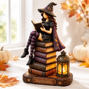 Könnte beinhalten: Eine Hexenfigur mit schwarzem Hut und Kleid sowie violett gestreiften Strümpfen, die lesend auf einem Bücherstapel sitzt. Neben den Büchern steht eine leuchtende Laterne auf einem Sockel, in dessen Vorderseite der Name Sabrina eingraviert ist.