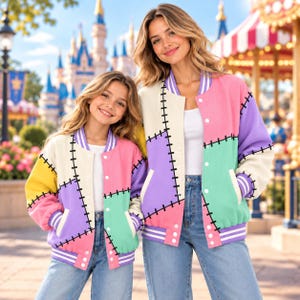 May include: Two matching varsity jackets featuring a patchwork design of cream, pink, purple, yellow, and mint green panels. The jackets have black stitched detailing along the seams, white snap buttons, and purple and white striped ribbed trim.