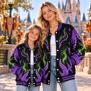 May include: A black varsity jacket featuring a vibrant purple and green flame pattern, stylized horn graphics, and white snap buttons. The jacket includes ribbed cuffs and a hem with purple stripes, worn over a white top and blue denim jeans.