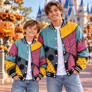 May include: Two matching varsity-style bomber jackets featuring a patchwork design of teal, yellow, and pink panels with black spiral and polka dot patterns. The jackets have white snap buttons, black and white striped ribbed cuffs, and collars.