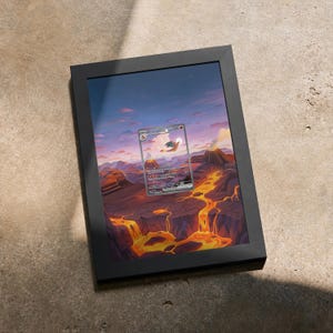 May include: A black rectangular frame containing a print of a Charizard ex trading card centered over a landscape illustration of a volcanic mountain range with flowing orange lava, rocky terrain, and a sunset sky with purple and blue clouds.