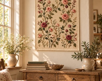 Puede incluir: Un tapiz rectangular que presenta un bordado intrincado de rosas rosas y rojas con hojas y tallos verdes sobre un fondo de tela color crema. La pieza de arte textil está suspendida de una varilla de madera con un cordel fino.