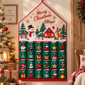 Könnte beinhalten: Ein hausförmiger Stoff-Adventskalender mit dem Text Merry Christmas Olivia. Er zeigt oben einen Schneemann, ein rotes Haus und ein Rentier sowie vierundzwanzig grüne Taschen, die von eins bis vierundzwanzig nummeriert und mit Symbolen verziert sind.