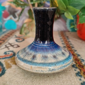 May include: A small, blue and white ceramic vase with a black rim. The vase has a rounded base and a narrow neck.