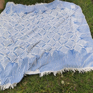 May include: A blue and white crocheted throw blanket with a fringe border. The blanket has a geometric pattern and is made of a soft, textured yarn.
