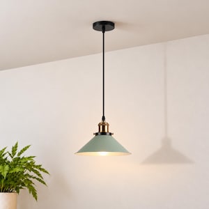 May include: A ceiling pendant light featuring a matte sage green conical metal shade, a brass-toned socket housing, and a thin black cord suspended from a circular black canopy. The light fixture emits a warm glow from the center.