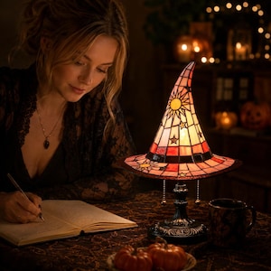 May include: A stained glass table lamp shaped like a witch hat, featuring a warm orange and red color palette with sun and star motifs. The lamp has a dark metal base and a pointed top, casting a soft glow on the surrounding table surface.