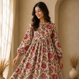 May include: A long-sleeved midi dress featuring a cream base with a repeating floral pattern in shades of pink, red, and olive green. The dress has a round neckline with a small tie closure, a gathered waistline, and full-length sleeves.