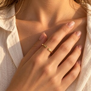Close-up of gold adjustable initial ring on finger showing engraved S and Z letters, beach background