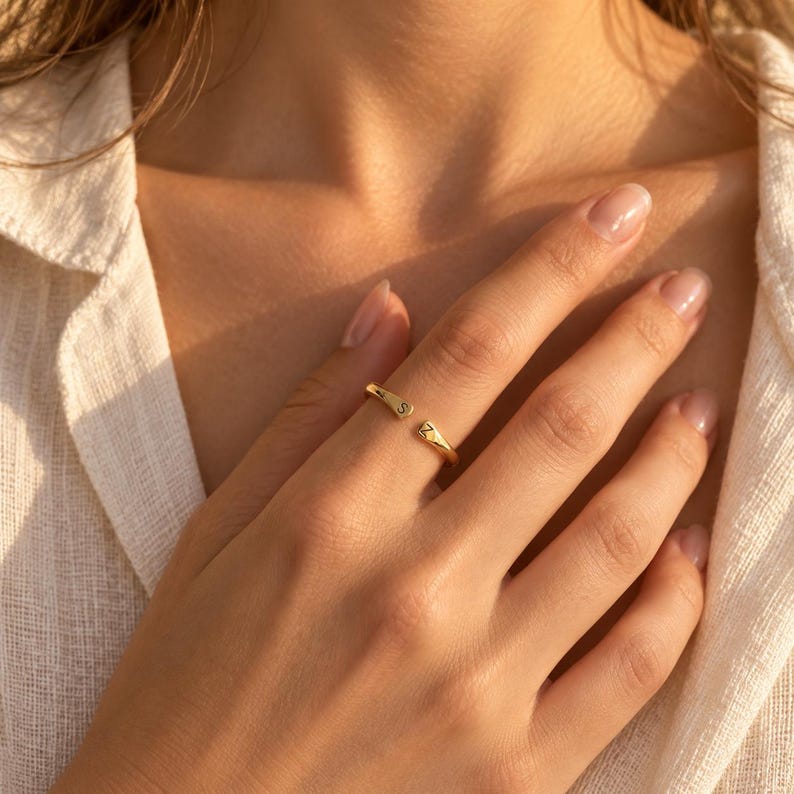 Close-up of gold adjustable initial ring on finger showing engraved S and Z letters, beach background