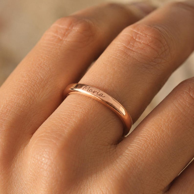 Close-up of a rose gold engraved name ring with the name Maria on a woman's finger