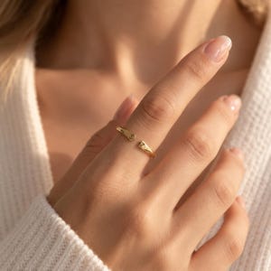 Woman wearing gold double initial open ring on finger, resting hand near collarbone in cream sweater