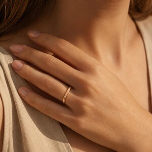 Op de afbeelding: Een dunne ring van ros&eacute;goud met een gladde, gepolijste afwerking. De ring is voorzien van een delicate, cursieve gravure op het buitenoppervlak met de tekst "Maria". Het metaal heeft een warme, roze metallic tint en een slank, rond ontwerp.