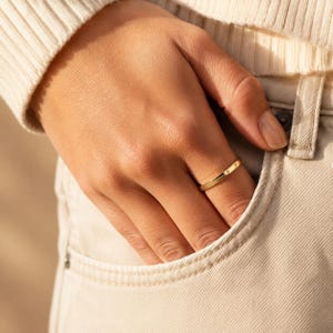 Woman wearing a gold engraved name ring with her hand in a denim pocket