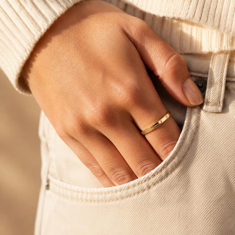 Woman wearing a gold engraved name ring with her hand in a denim pocket