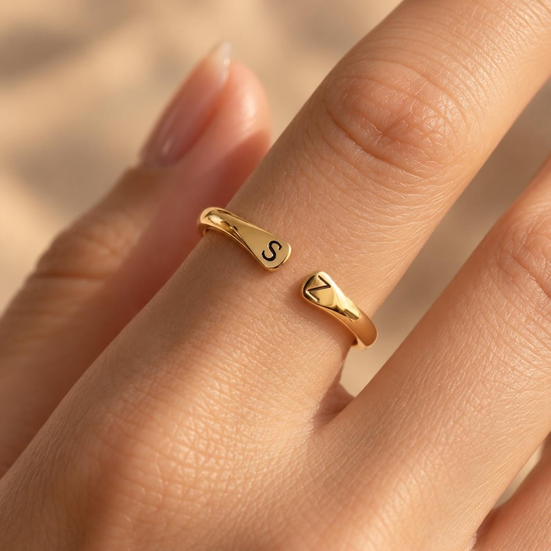 Gold plated adjustable double initial ring with S and Z letters on teardrop tips, flat lay on natural stone