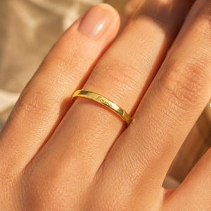 Woman wearing a gold plated engraved name ring resting her hand on her shoulder