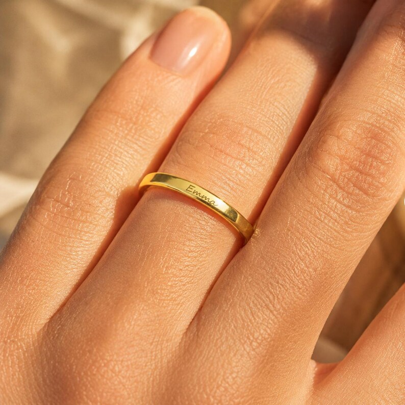 Woman wearing a gold plated engraved name ring resting her hand on her shoulder