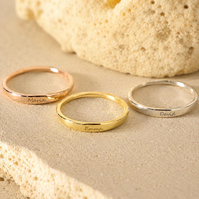 Three personalized engraved name rings in rose gold, gold and sterling silver with the names Maria, Emma and David