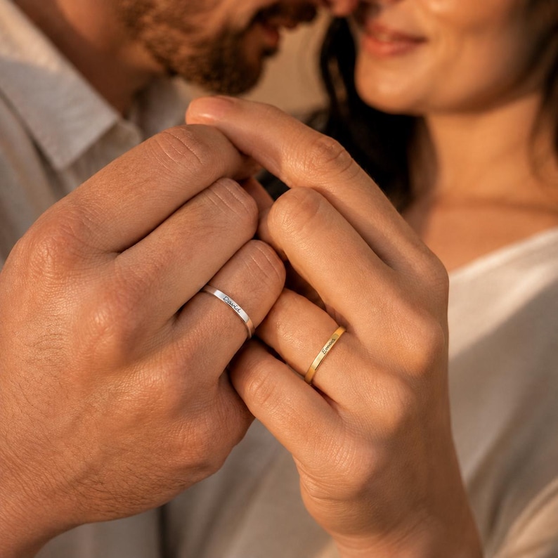 Couple holding hands wearing matching engraved name rings personalized with David and Emma