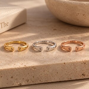 Three custom double initial rings in gold, silver and rose gold finishes lined up on stone shelf