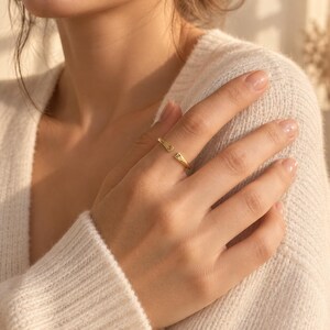 Woman's hand with gold double initial ring resting on chest, wearing white linen shirt in sunlight