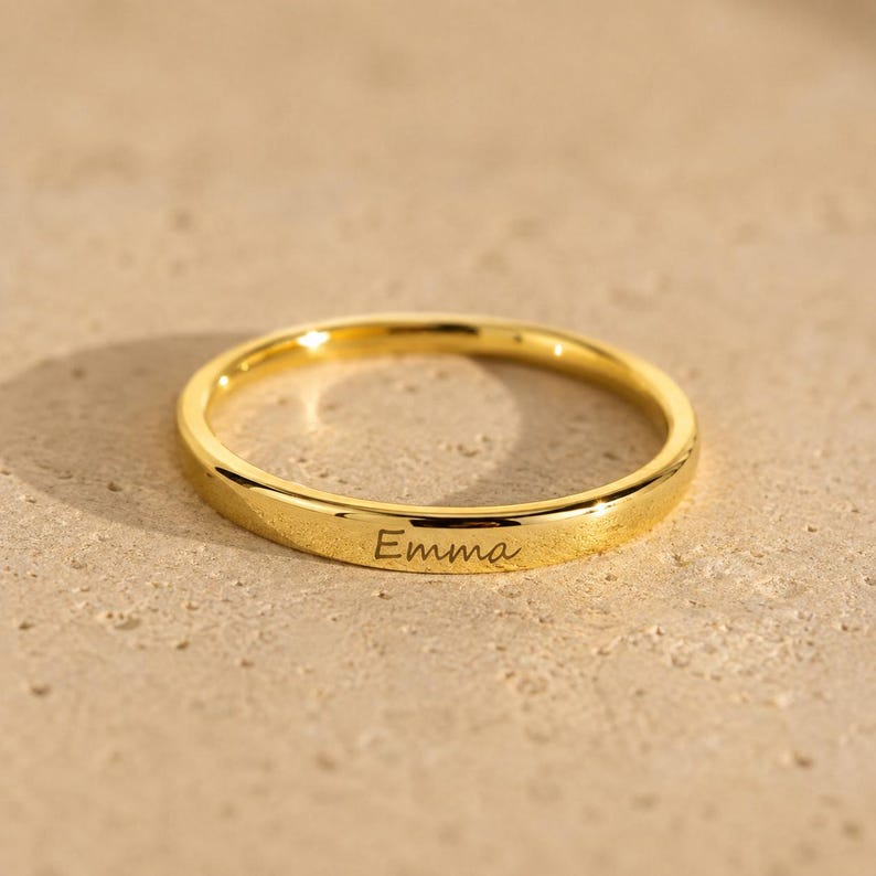 Gold engraved name ring personalized with the name Emma displayed on a neutral stone surface