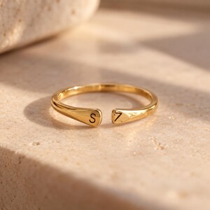K&ouml;nnte beinhalten: Ein goldfarbener offener Ring mit polierter Oberfl&auml;che, der auf einem Ende den Buchstaben S und auf dem anderen Ende den Buchstaben Z eingraviert hat. Die Ringschiene ist glatt und verj&uuml;ngt sich leicht zur &Ouml;ffnung hin, wo die Buchstaben liegen.