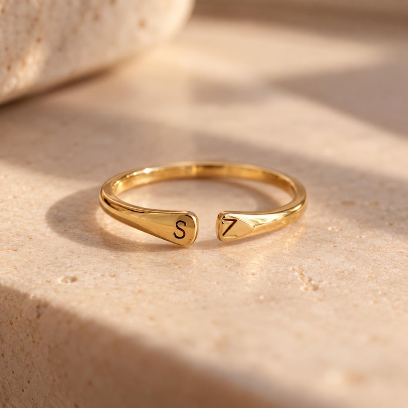 K&ouml;nnte beinhalten: Ein goldfarbener offener Ring mit polierter Oberfl&auml;che, der auf einem Ende den Buchstaben S und auf dem anderen Ende den Buchstaben Z eingraviert hat. Die Ringschiene ist glatt und verj&uuml;ngt sich leicht zur &Ouml;ffnung hin, wo die Buchstaben liegen.