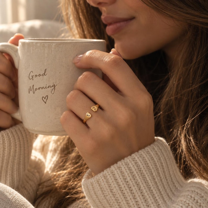 Woman wearing gold double initial ring while holding a mug that reads Good Morning